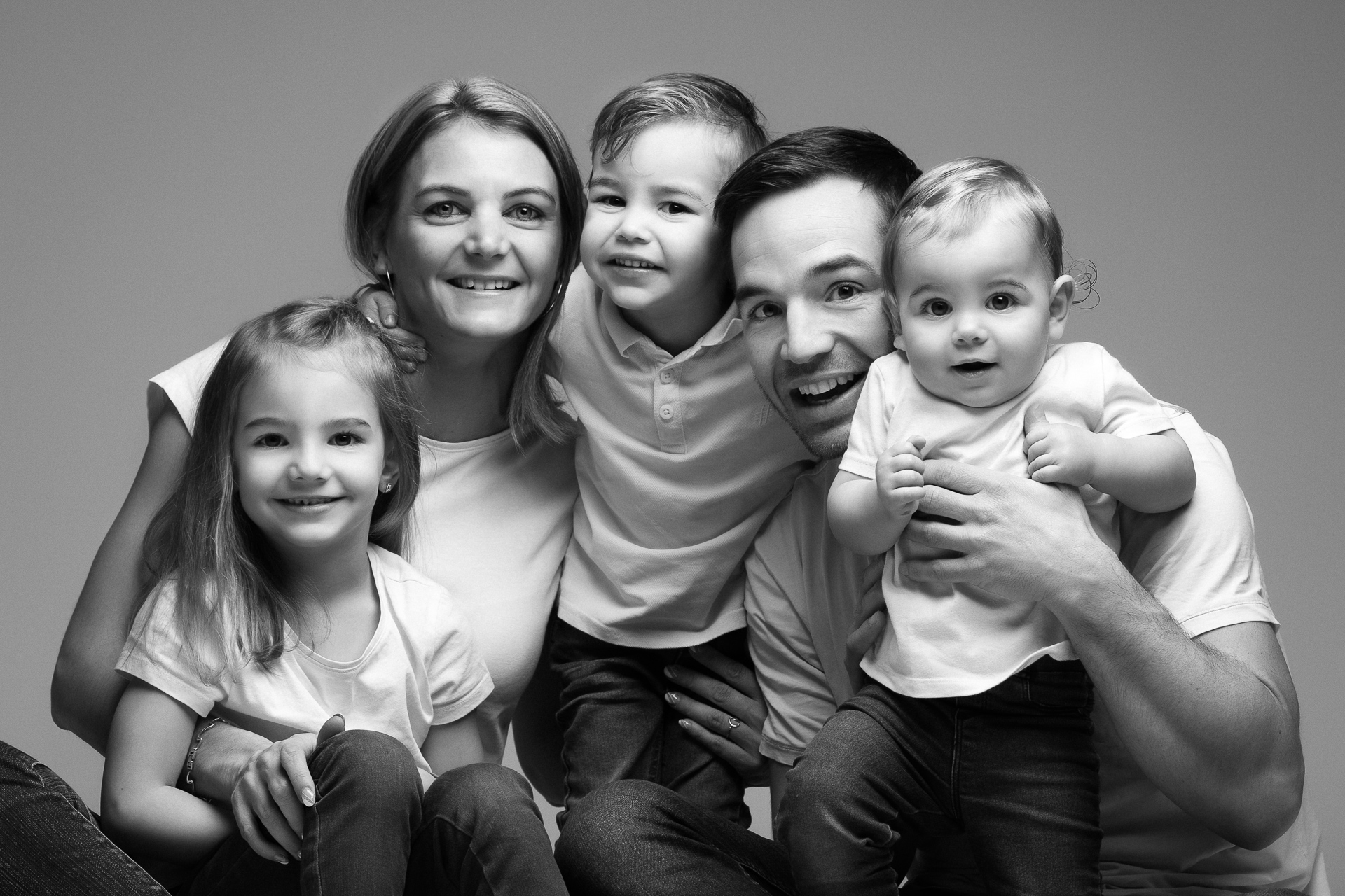 Portrait d'une famille avec 3 enfants dont un bébé de quelques mois, mise en N&B pour faire ressortir uniquement les émotions