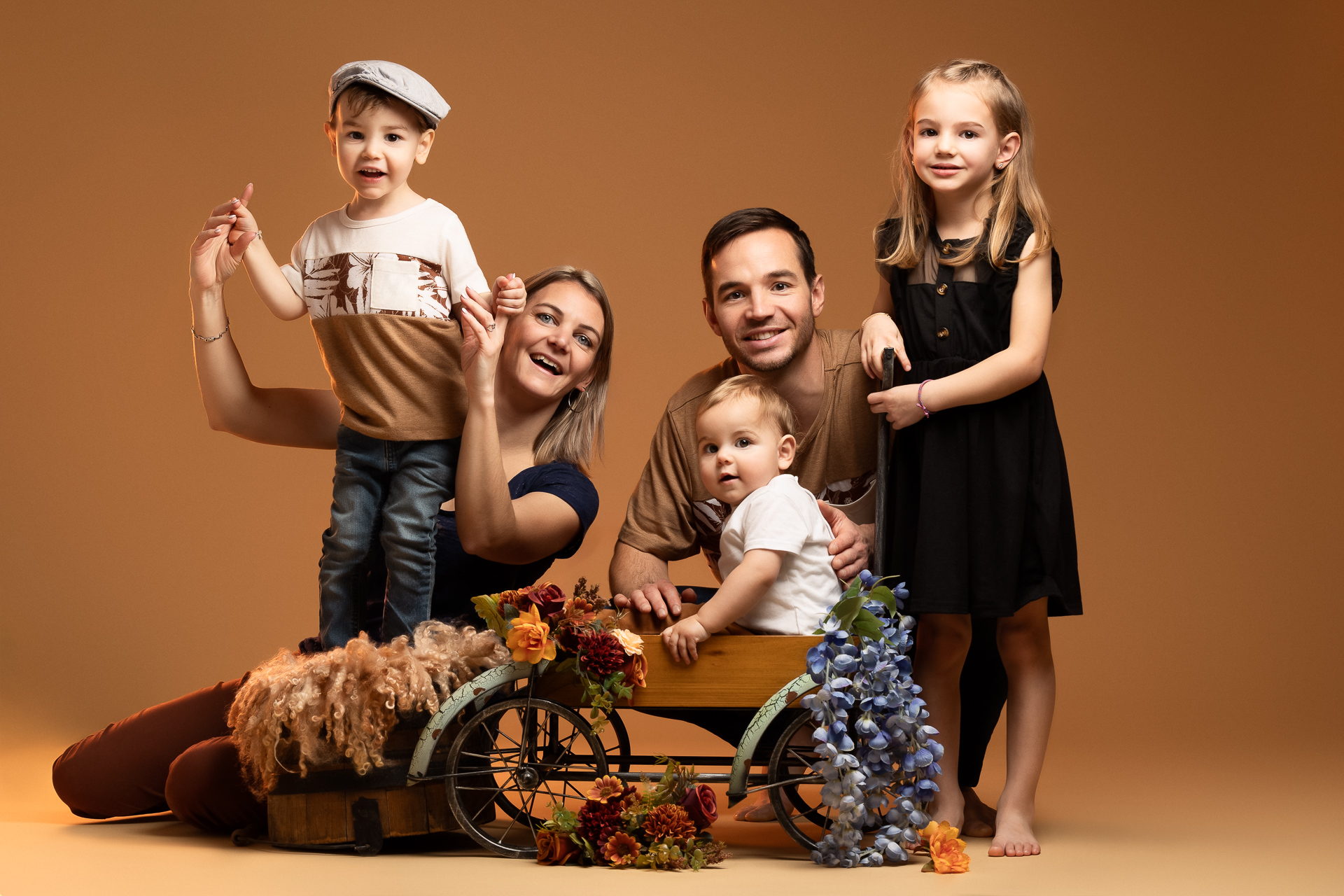 Portrait de famille en action, dans un décor simple, tous ensemble, deux parents et 3 enfants dont un bambin