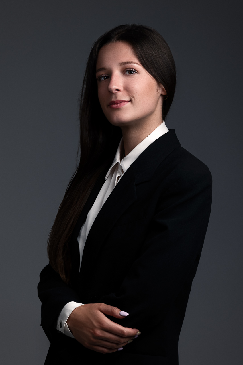 Portrait professionnel d'une jeune femme en blazer noir sur fond gris, réalisé par Estelle, photographe professionnelle à Pusignan (69)