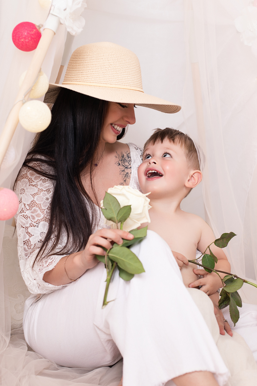 Maman et enfant riant avec une rose blanche dans le tipi — séance photo Fête des Mères 2026 Studio Evidence Pusignan