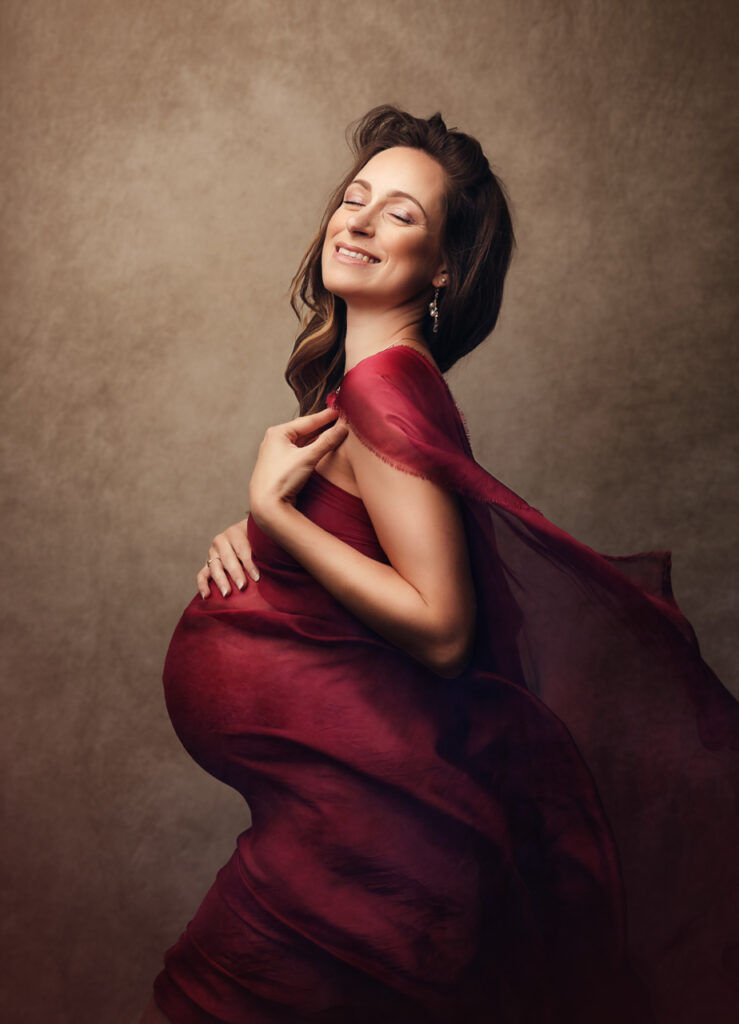 Séance grossesse studio — femme enceinte enveloppée de soie bordeaux, photographiée par Aurélie Perillou